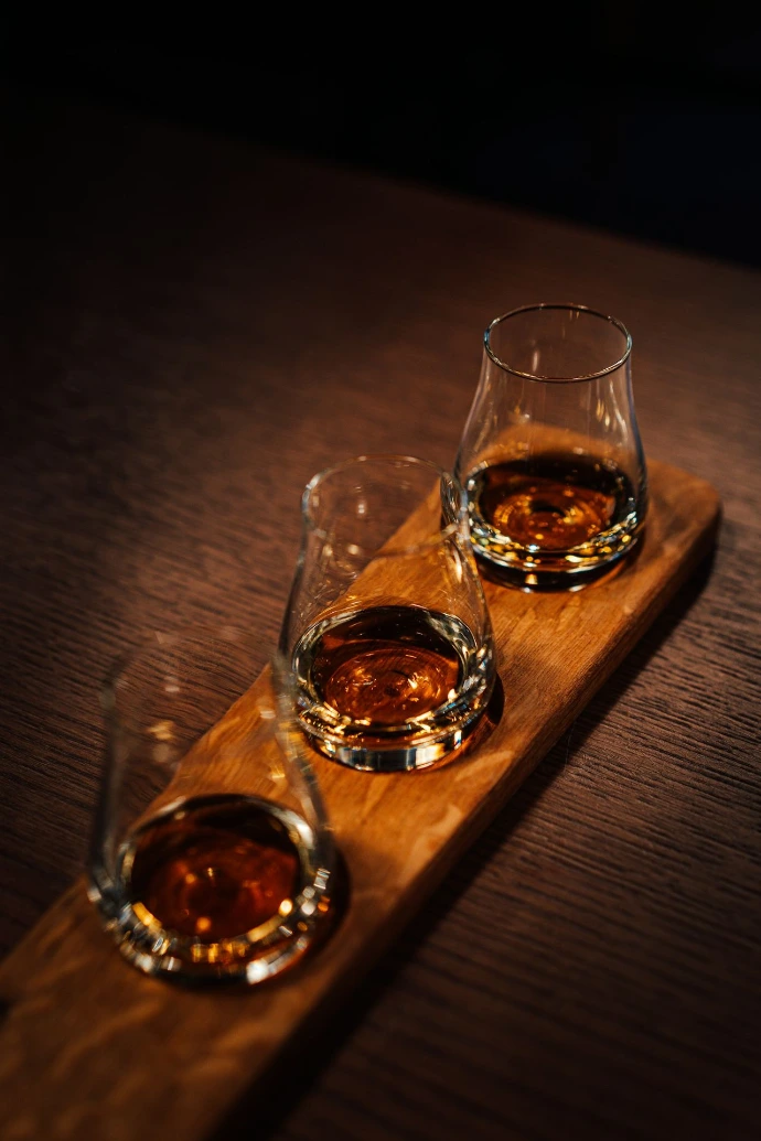 Three glasses of whiskey sitting on a wooden tray